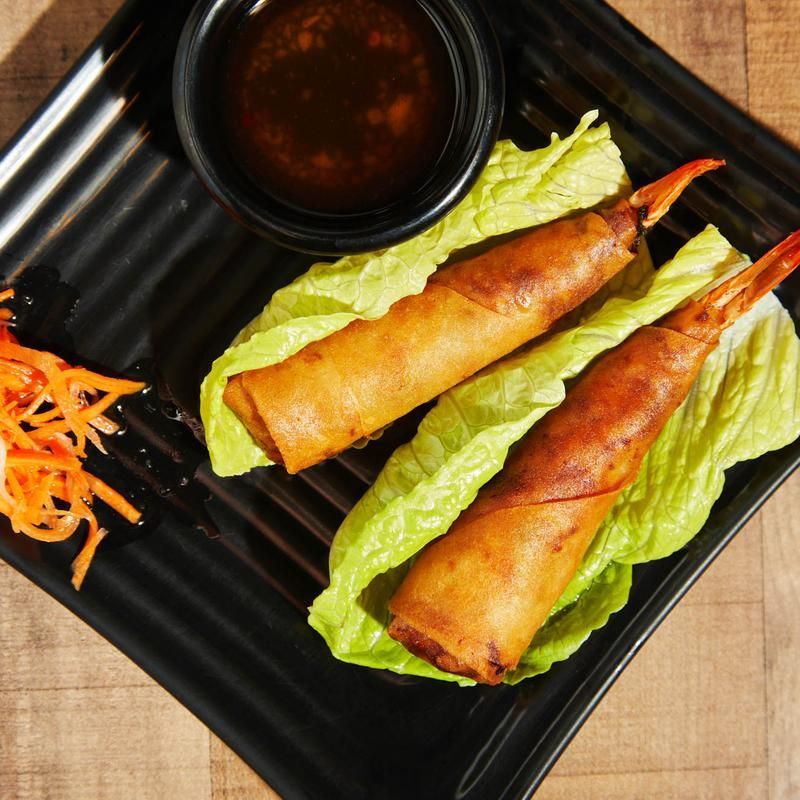 Two fried spring rolls on lettuce with dipping sauce and shredded carrots on a black plate.