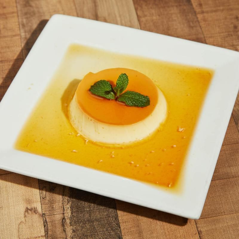 Custard dessert with orange sauce and mint on a white square plate