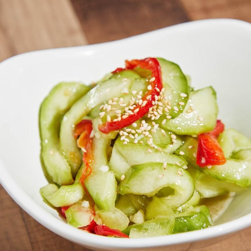 Sliced cucumber salad with red peppers and sesame seeds in a white bowl