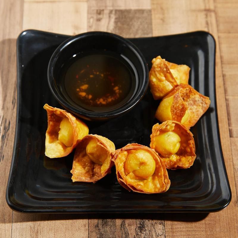Black plate with fried dumplings and a small bowl of dipping sauce on a wooden table