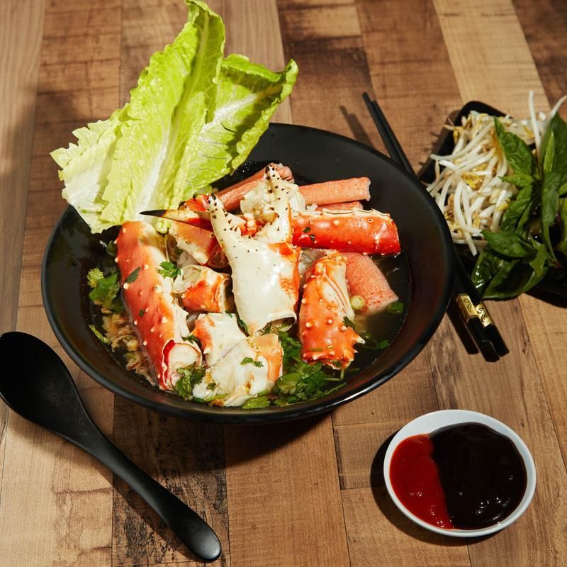 Korean seafood salad with crab legs, lettuce, noodles, and dipping sauce on a wooden table