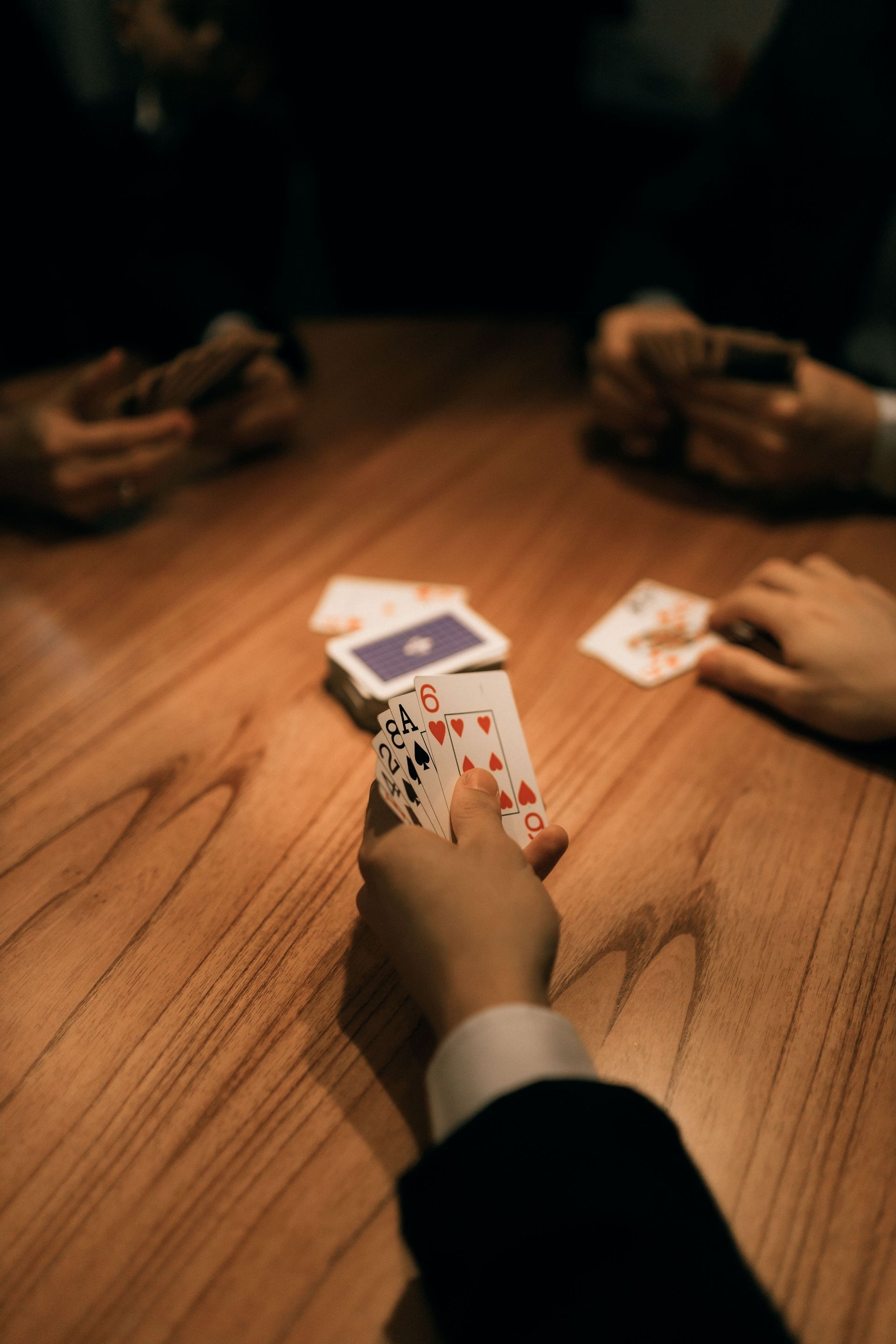 Een groep ouderen speelt kaart rond een houten tafel in een zonnige kamer.