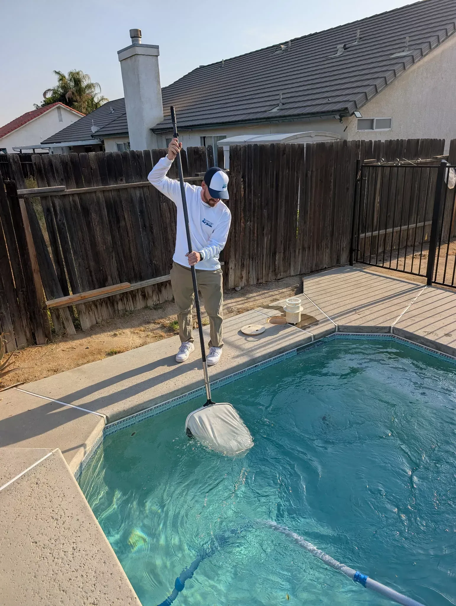 Chris Hurst skimming a backyard pool during a weekly pool service visit in Bakersfield