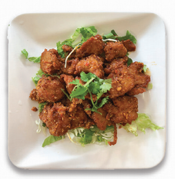 Plate of crispy fried chicken bites on lettuce, garnished with cilantro on a white square plate