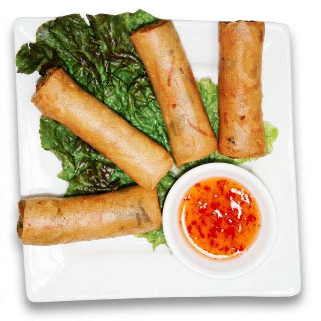 Four golden fried spring rolls on greens with a small cup of red dipping sauce on a white plate