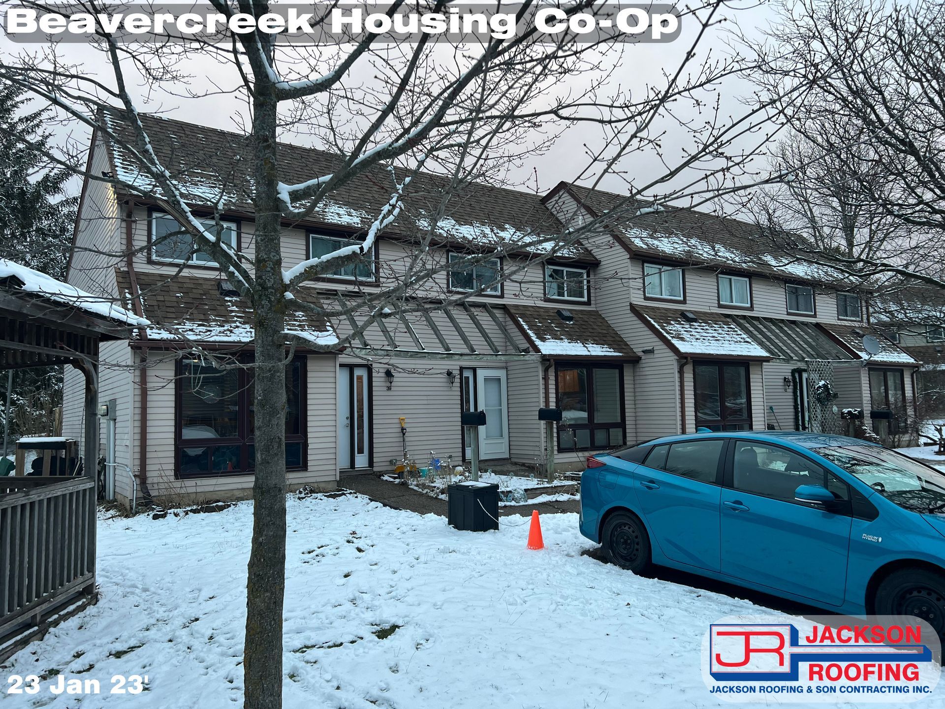 A blue car is parked in front of a house that is covered in snow.