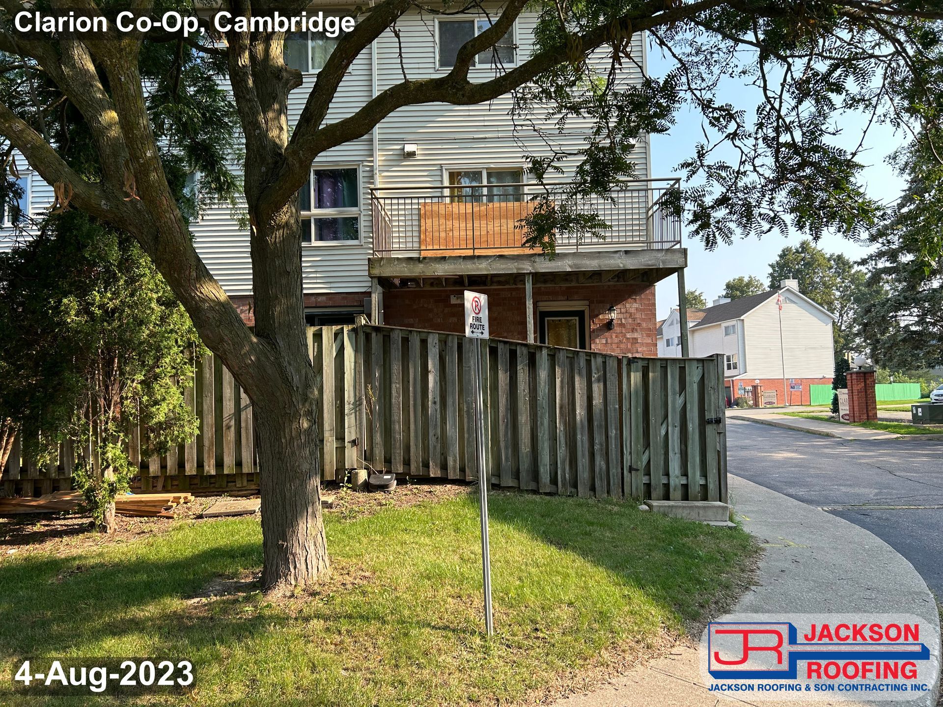 A house with a wooden fence and a tree in front of it.