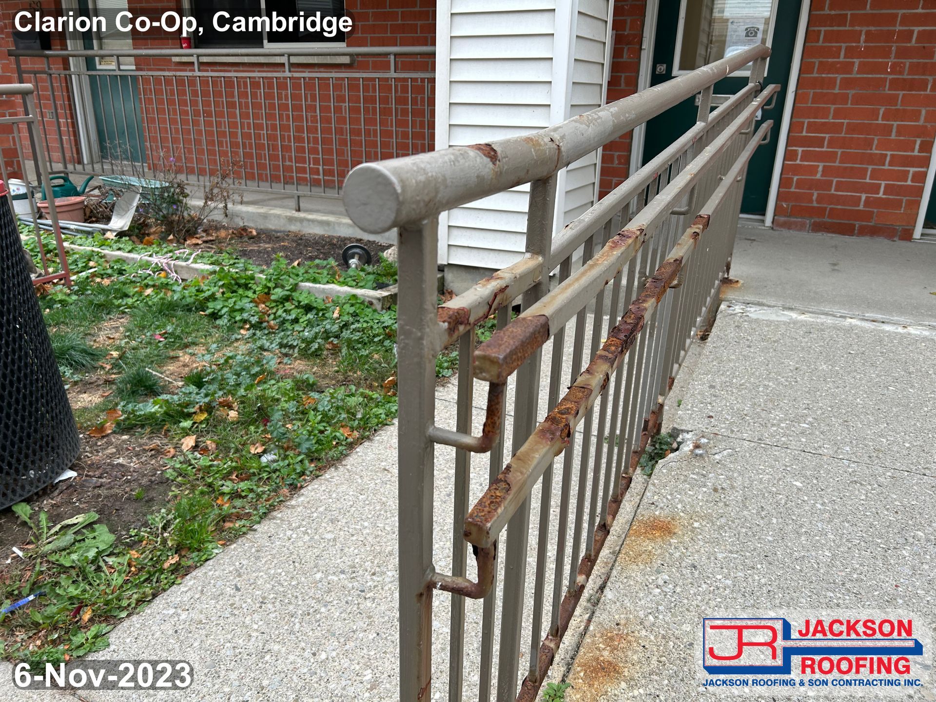 A rusty railing on a sidewalk next to a brick building.