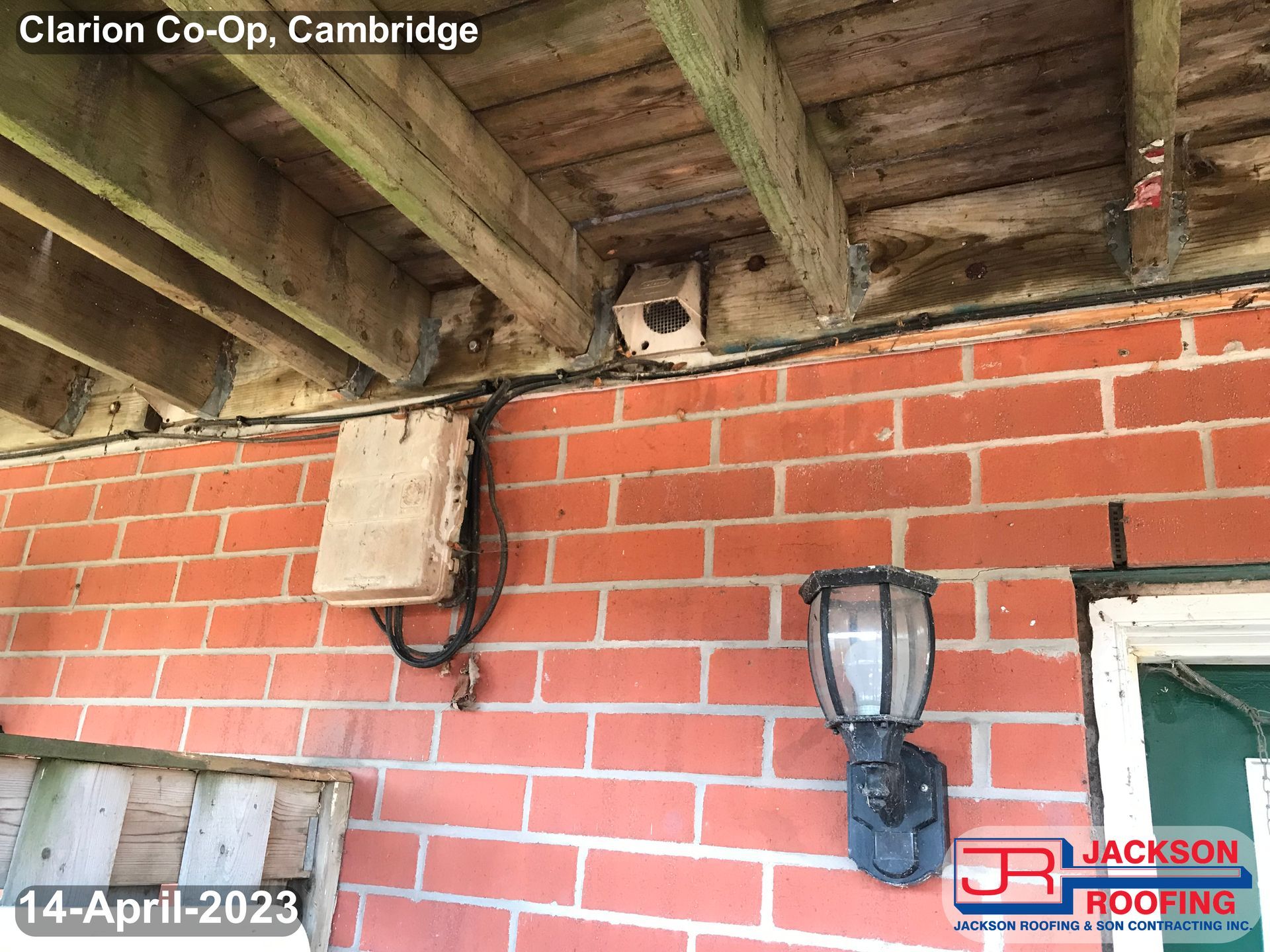 A brick wall with a lamp and a wooden roof.