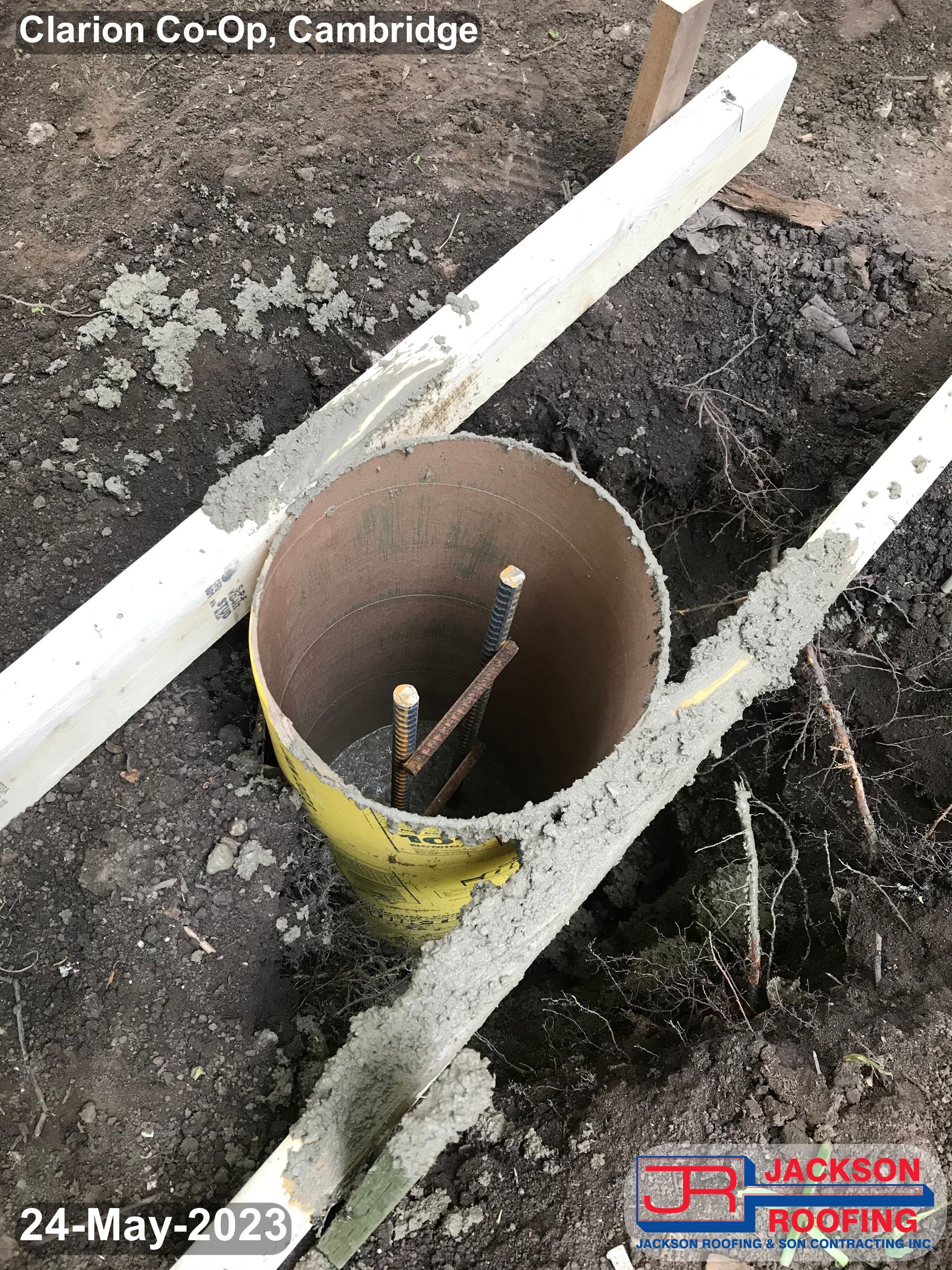 A yellow pipe is sitting in the dirt next to a wooden pole.