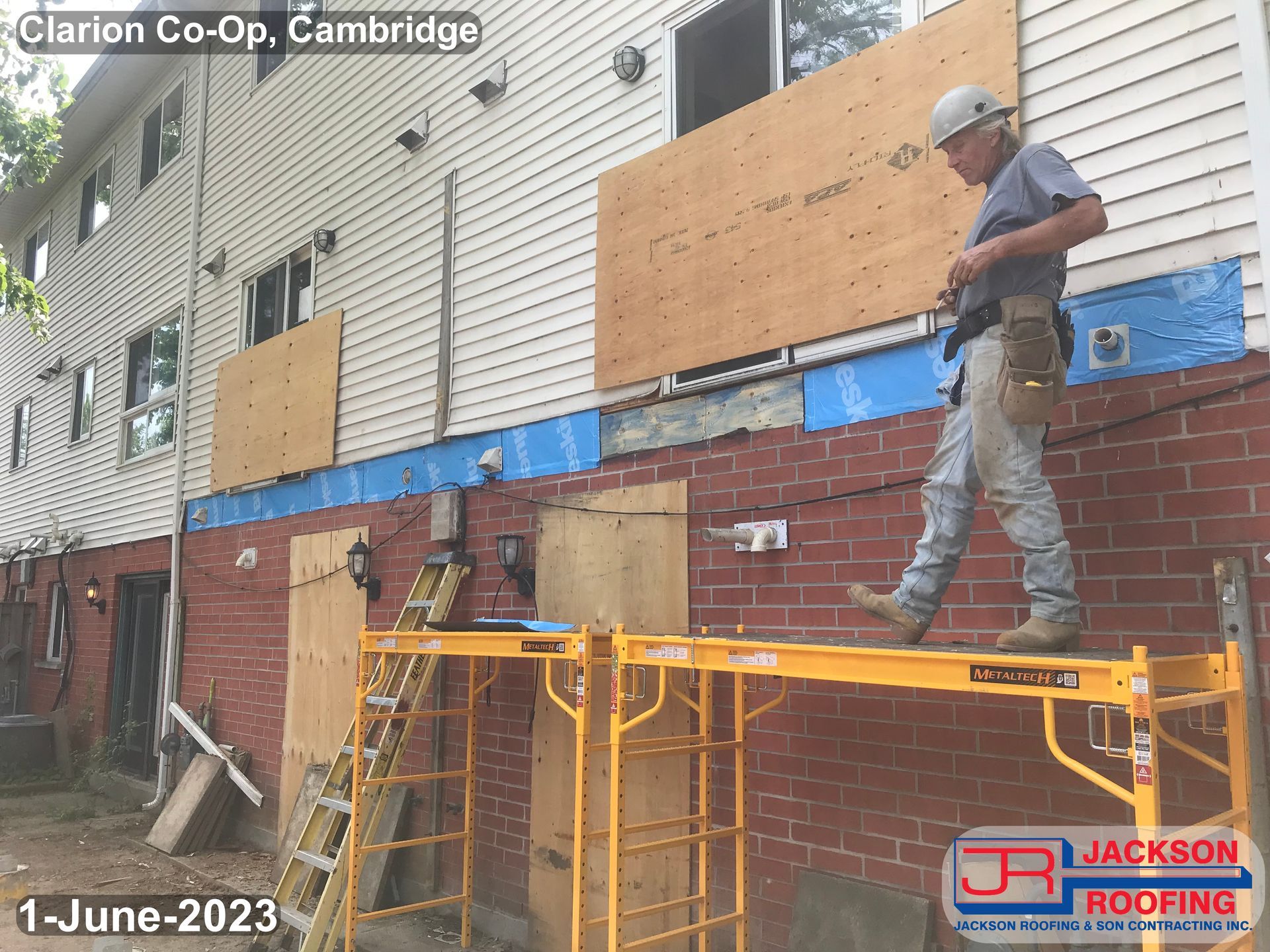 A man is standing on a scaffolding in front of a brick building ..