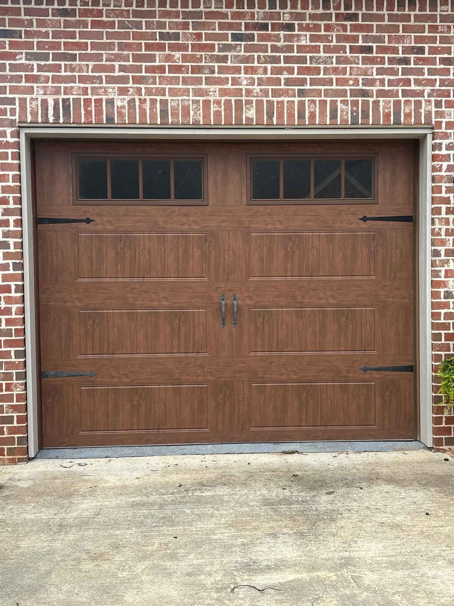 Brown garage door with windows, set in a red brick building. Concrete surface in front.