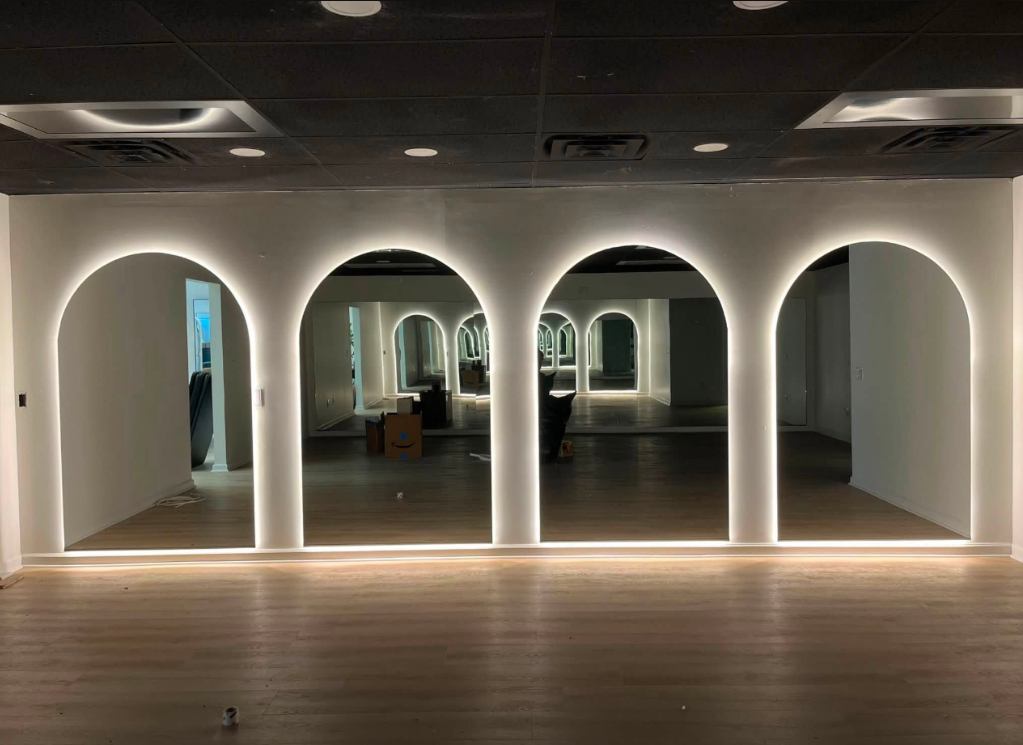 Modern interior with arched doorways, mirrored walls, and warm accent lighting over wood flooring.