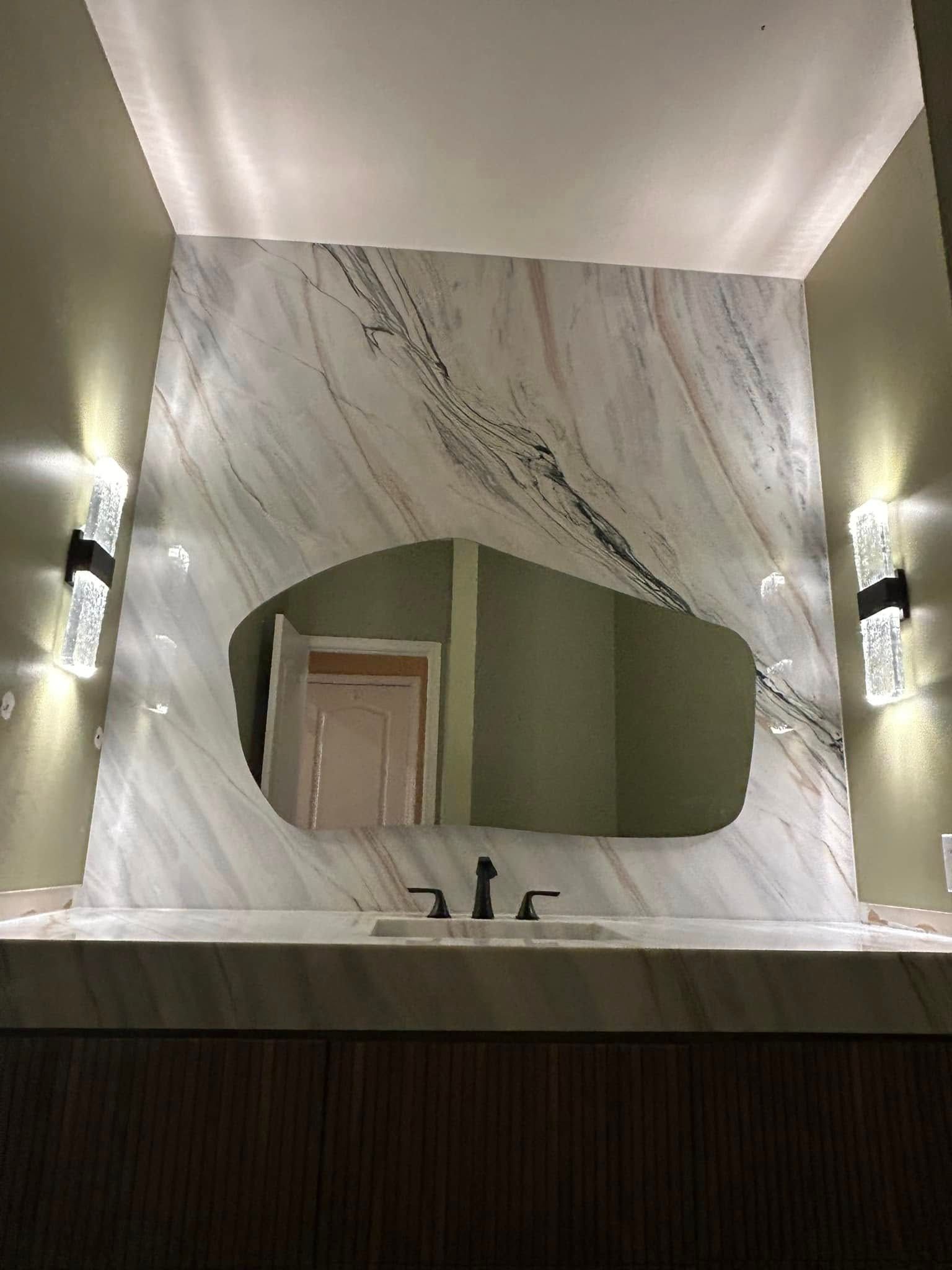 Marble bathroom vanity with oval mirror, wall sconces, and a sink beneath a recessed lighted alcove
