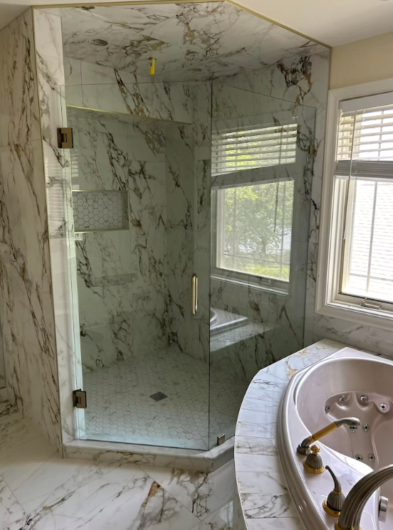 Glass shower enclosure beside a marble bathtub in a bright, white bathroom