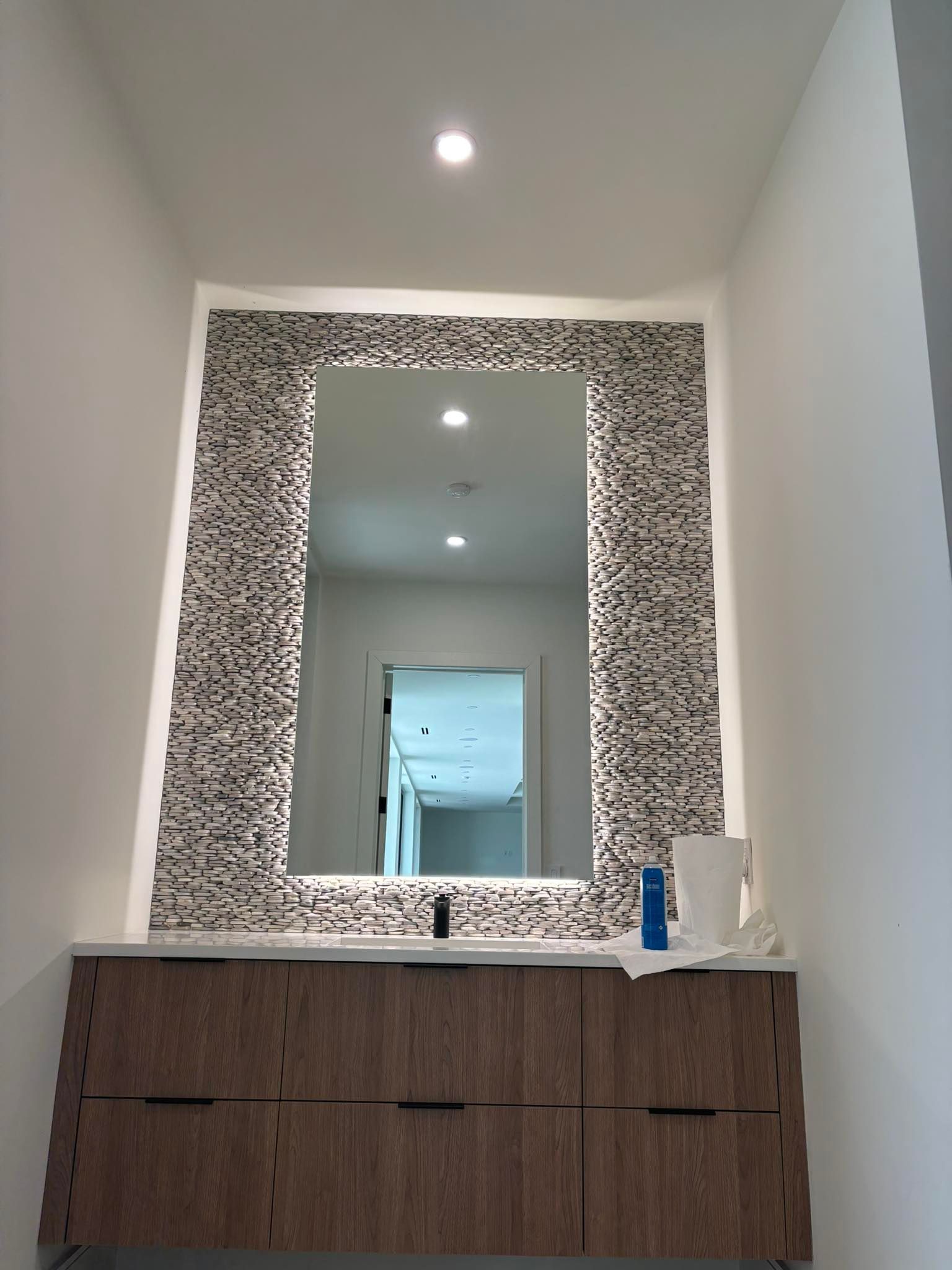 Bathroom vanity with wood cabinets, white sink, and large framed mirror beneath recessed ceiling lights.