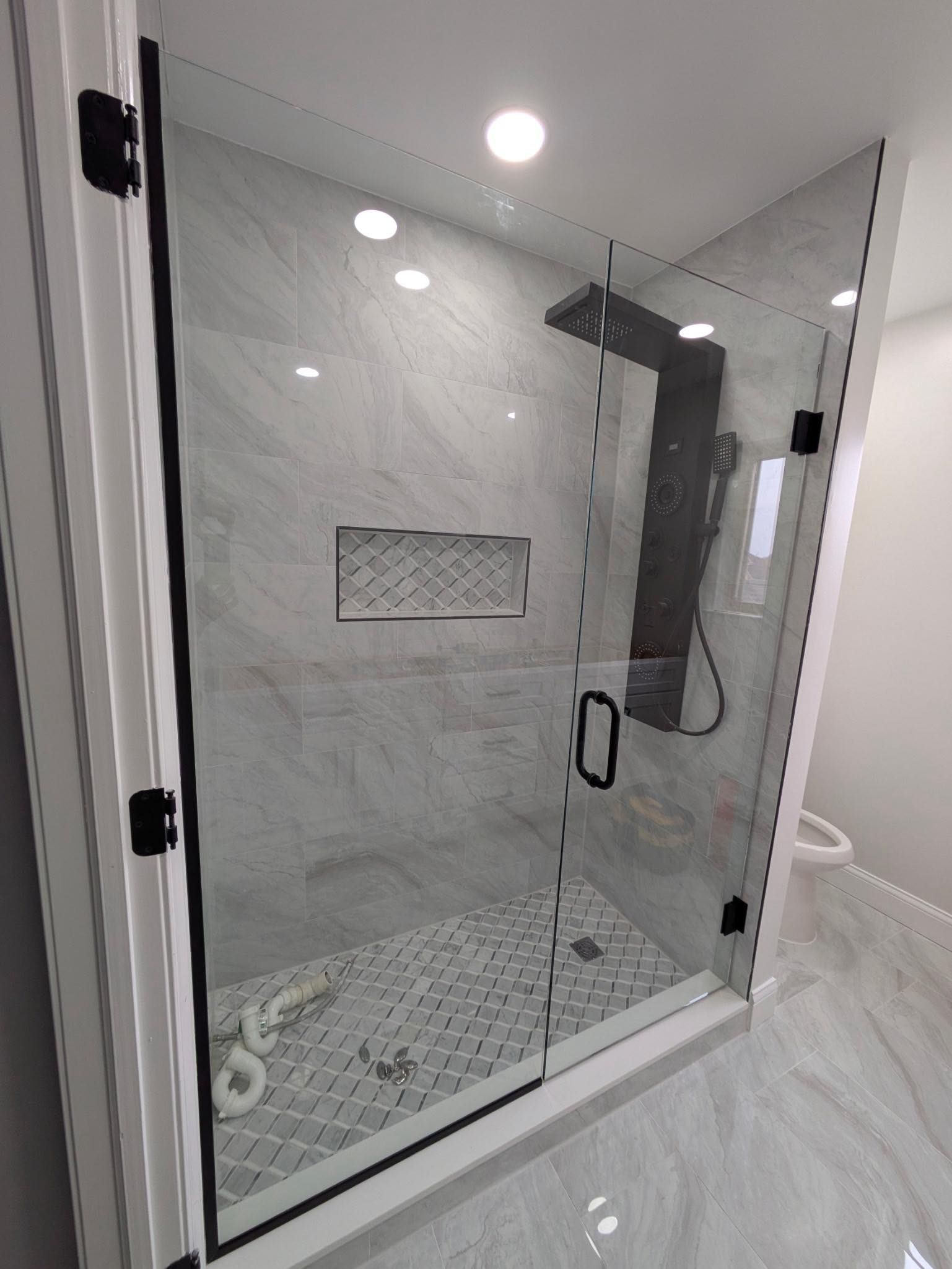 Modern white-tiled shower with glass door, built-in shelf, and black rainfall showerhead