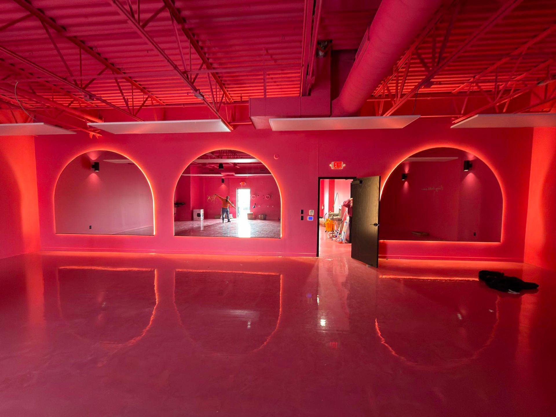 Red-lit empty room with arched wall openings, polished floor, and exposed ceiling beams