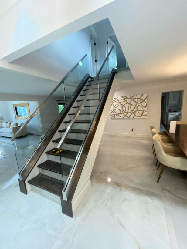 Modern living room with a black staircase, beige sofa, and white tile floor.