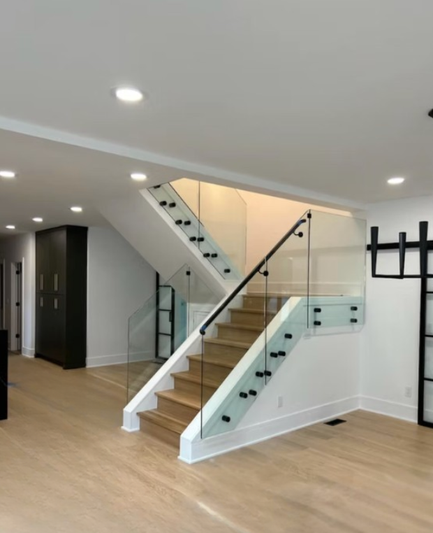 Modern home interior with open staircase, glass railing, and light wood floors