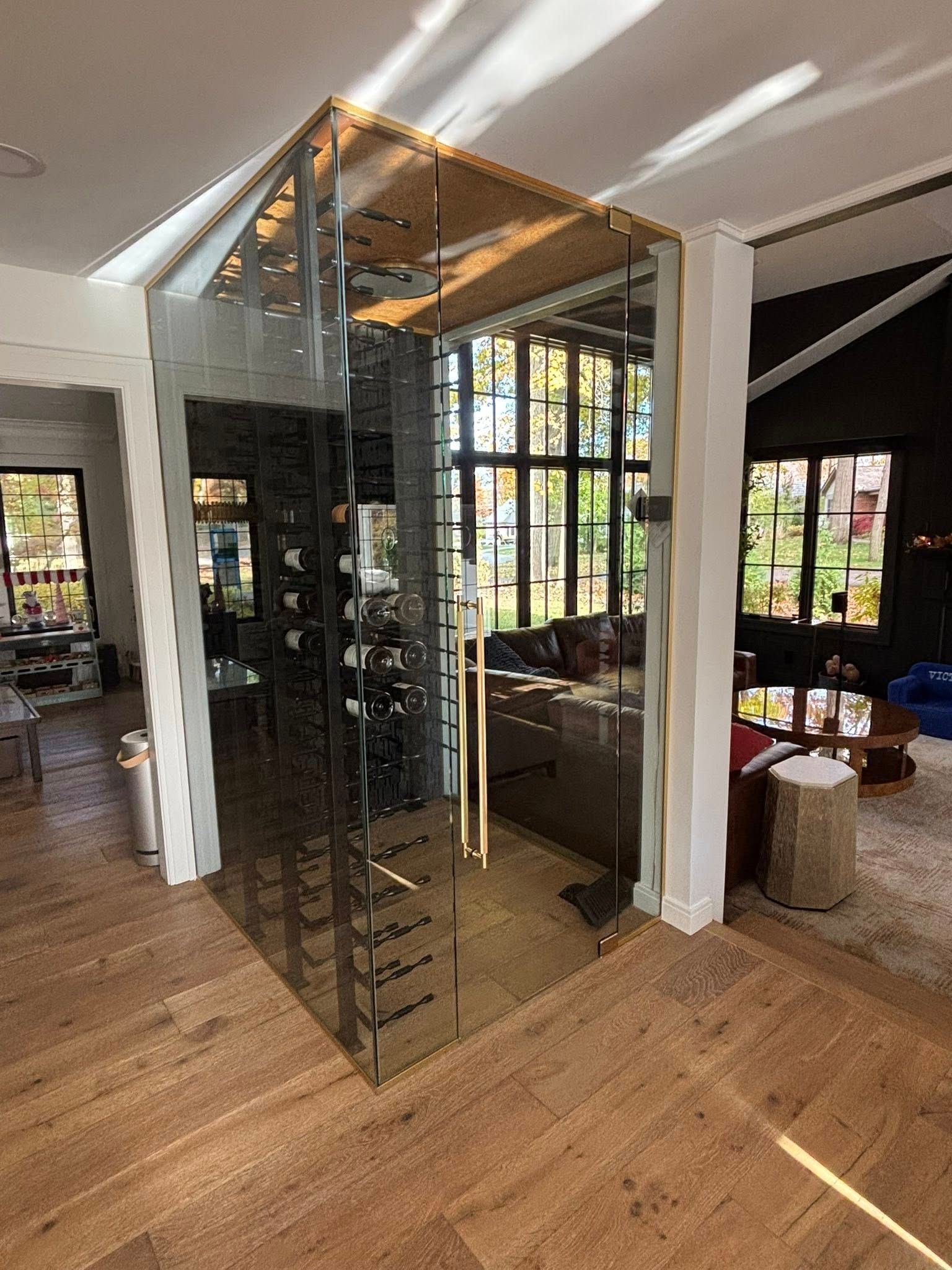 Modern home interior with a glass elevator shaft beside large windows and hardwood floors