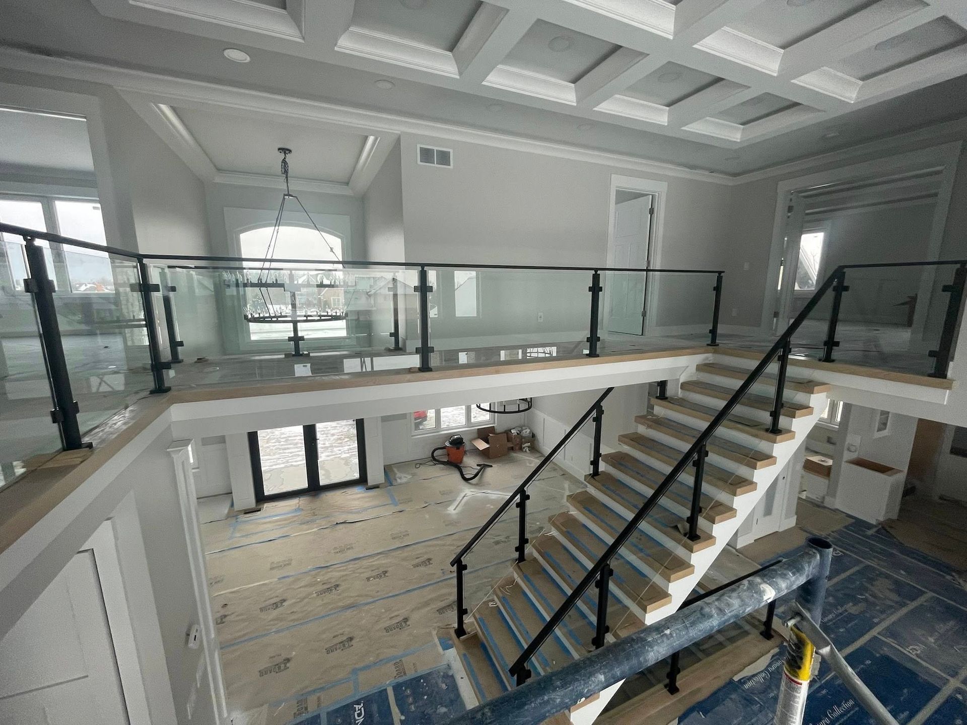 Modern foyer with glass-railed mezzanine and staircase, white walls, and marble floor