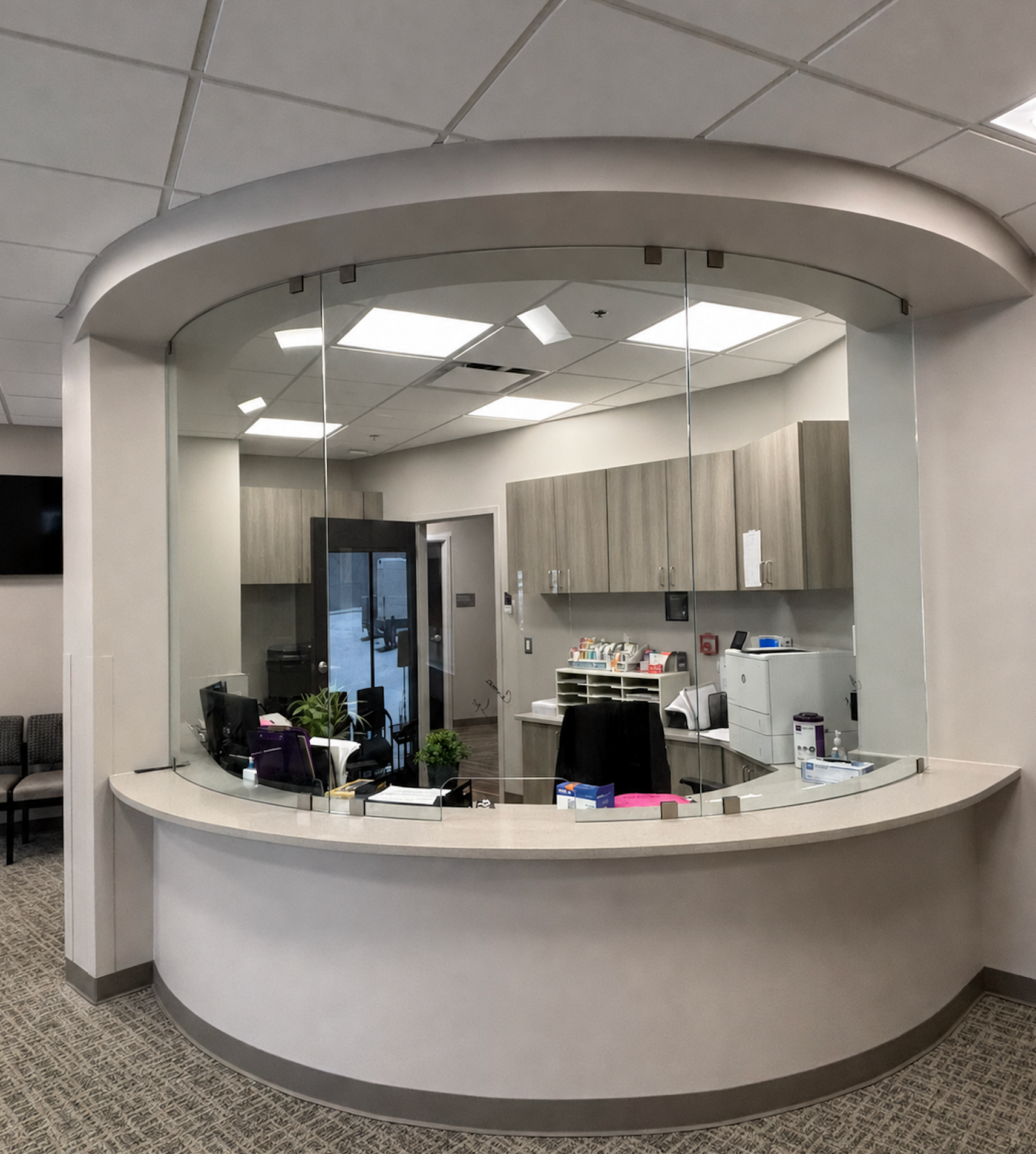 Curved reception desk in a bright office lobby with cabinets, computer equipment, and overhead lighting