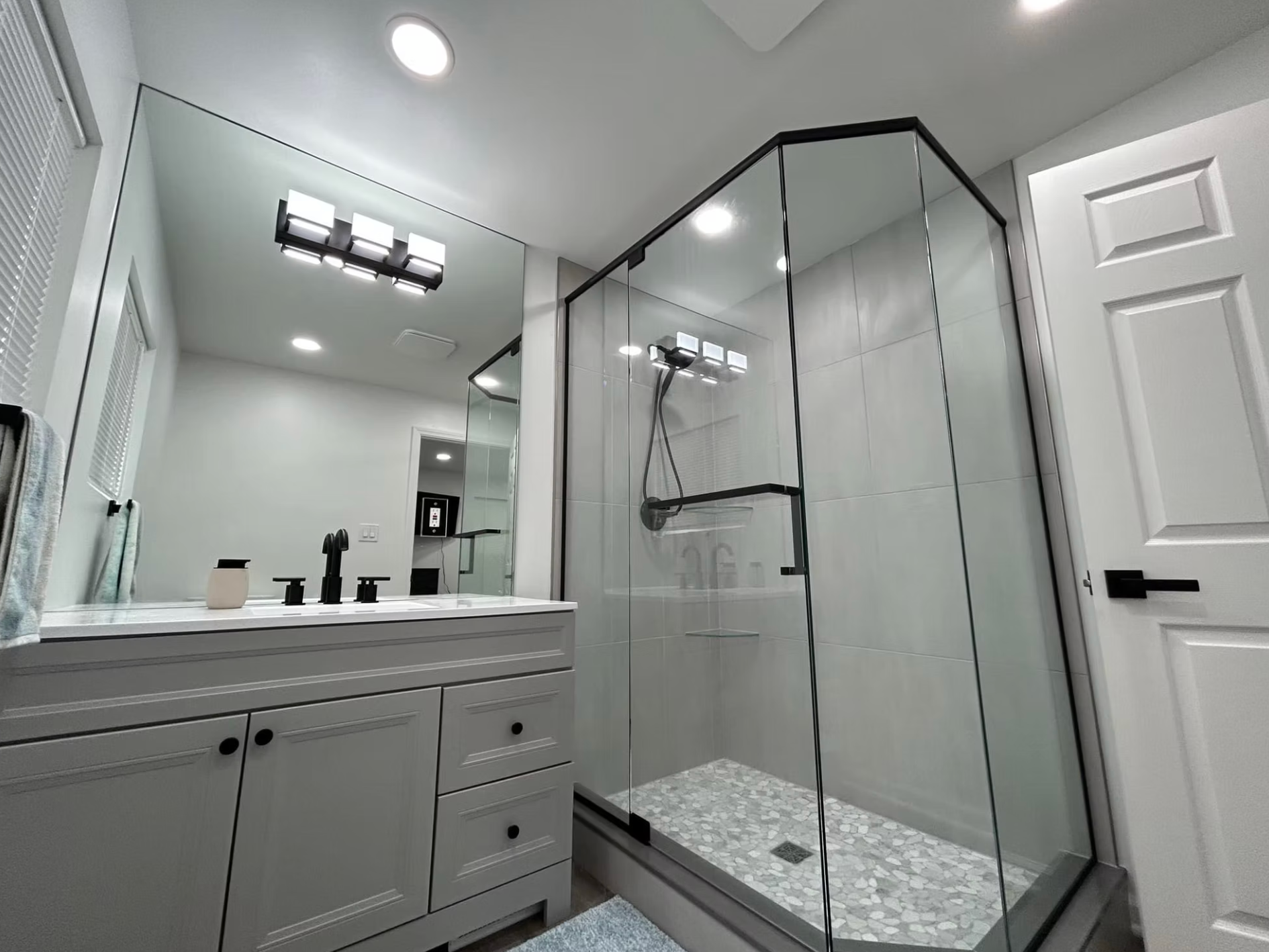 Bright modern bathroom with double vanity, mirrors, and glass-enclosed shower with patterned tile floor