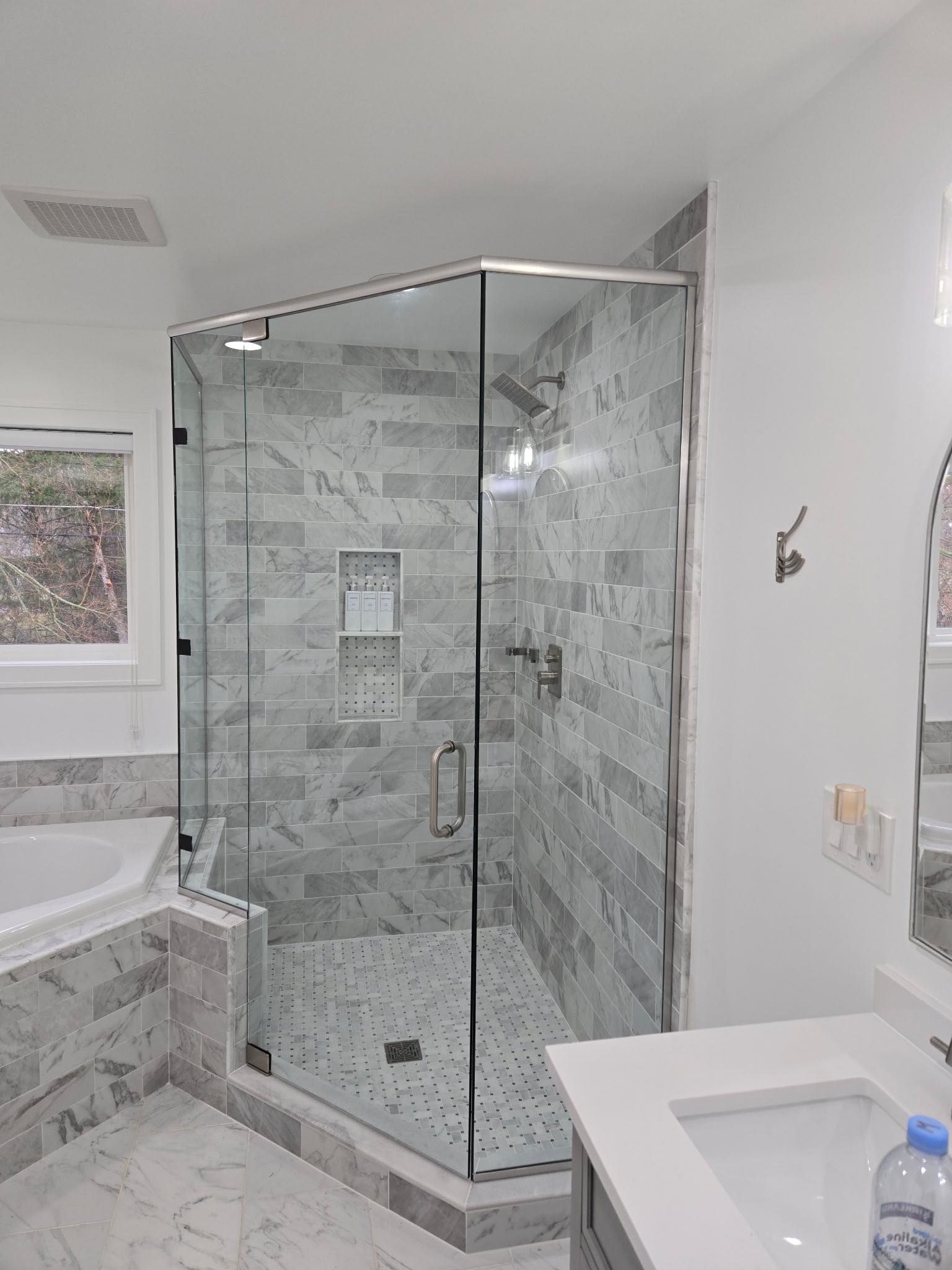 Modern bathroom with glass corner shower, marble tile, white vanity, and bathtub.