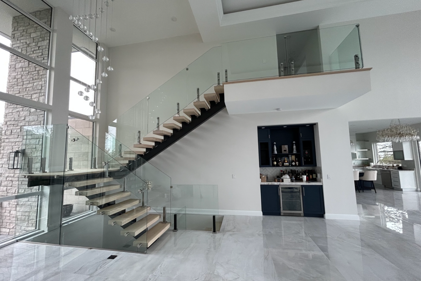 Modern open-concept interior with floating staircase, glass railings, and white marble floors