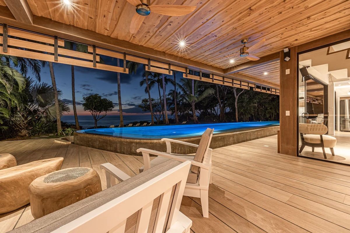 Terrasse en bois avec piscine au crépuscule ; sièges extérieurs, plafond en bois, vue sur l'océan sombre.