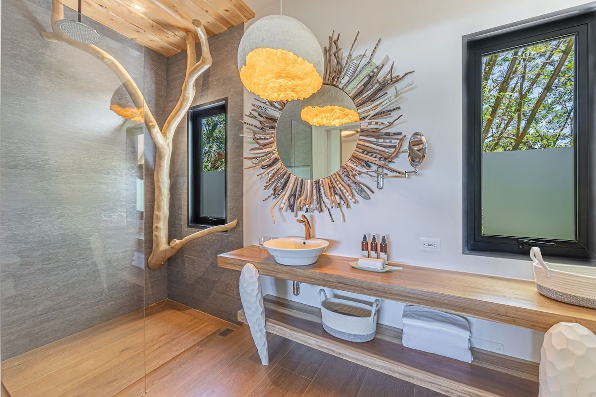 Salle de bains avec meuble-lavabo en bois, miroir décoratif et petites fenêtres. Une branche d'arbre orne le mur.