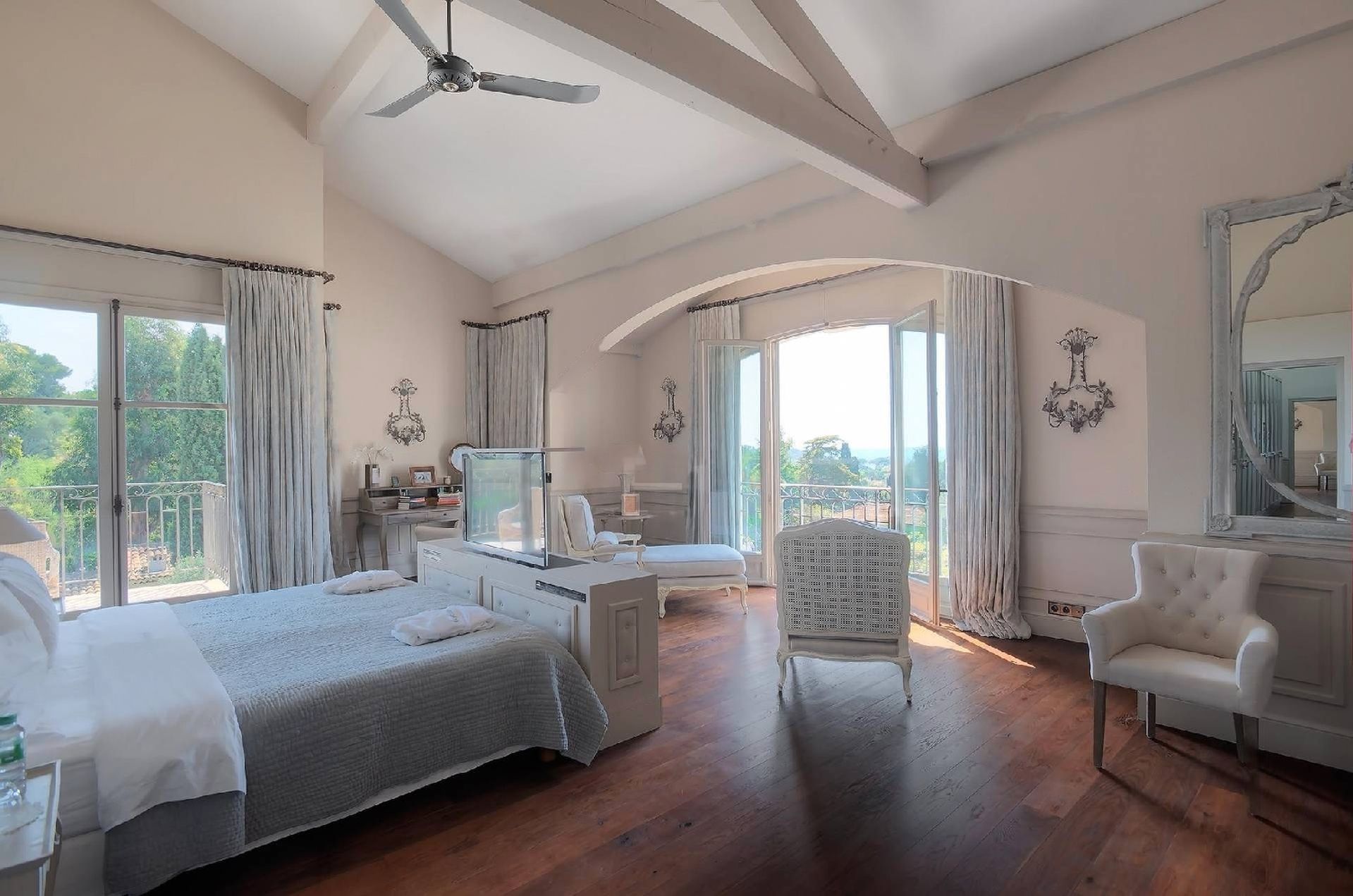 Chambre spacieuse avec parquet, grandes fenêtres et mobilier blanc, comprenant un lit, une chaise et un berceau.