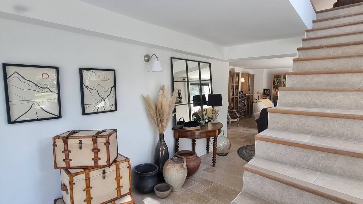 Entrée avec escalier, malles, tableaux encadrés, grand miroir et vases décoratifs dans une maison moderne et lumineuse.
