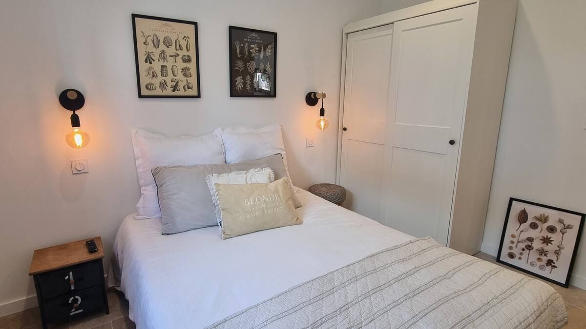 Chambre avec un lit blanc, des coussins décoratifs, des appliques murales, des posters et une armoire.