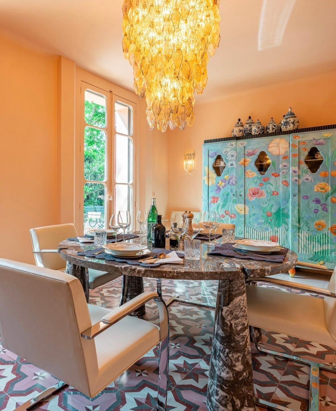 Salle à manger élégante avec lustre, table en marbre, paravent coloré et chaises couleur crème.