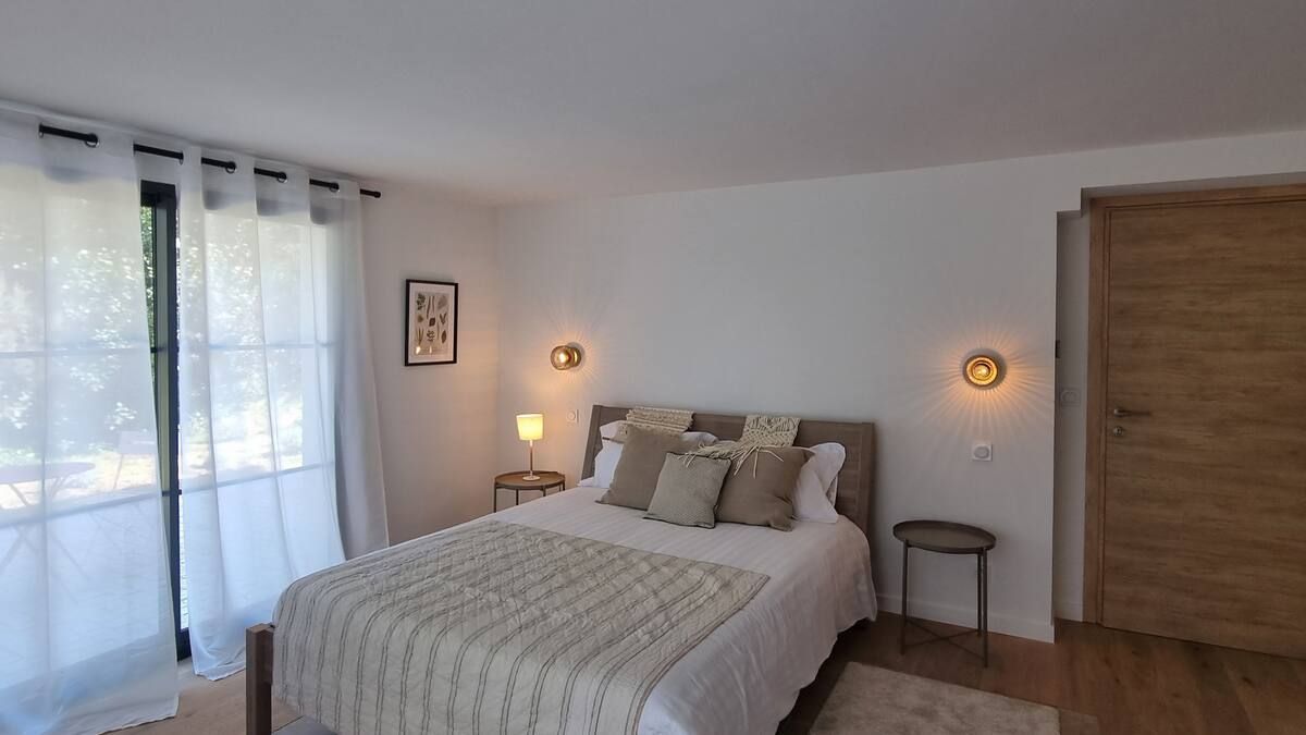 Chambre avec un lit, deux tables de chevet, des appliques murales, une fenêtre et une porte.