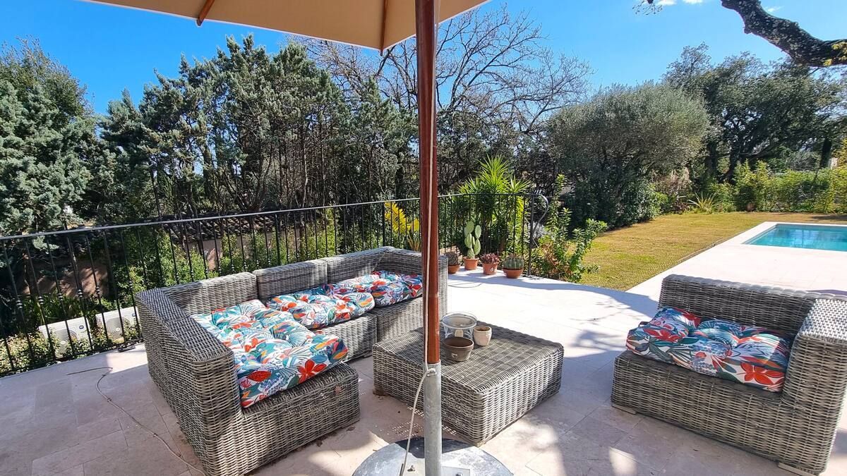 Mobilier de patio avec coussins colorés sous un parasol, près d'une piscine et de verdure.