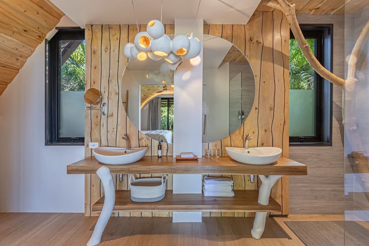 Salle de bains avec lambris clair, double vasque avec lavabos circulaires et grand miroir rond.
