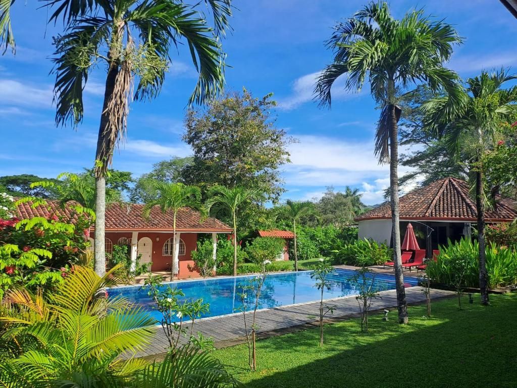 Piscine dans un cadre tropical ; un bâtiment au toit de tuiles rouges se dresse en arrière-plan. Couverture de piscine bleue. Étiquette « CO-EXCLUSIVITÉ ».