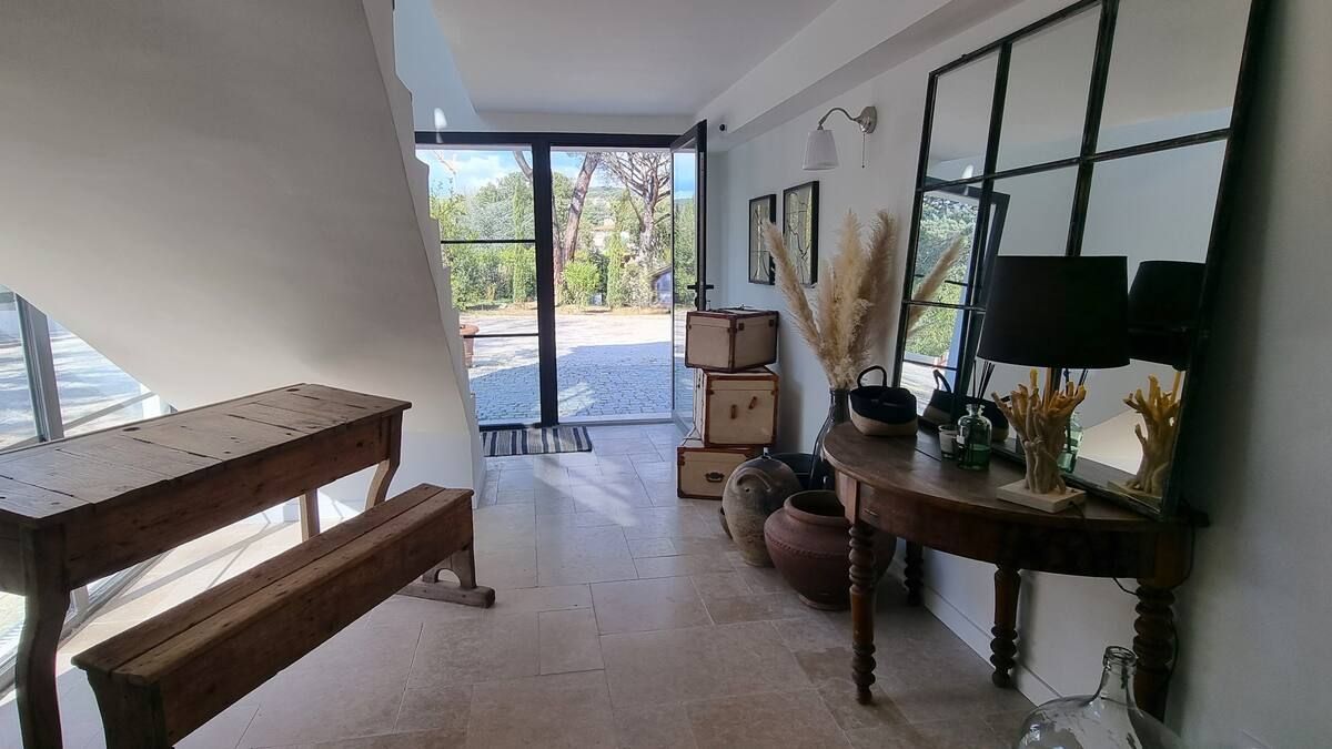 Couloir avec un banc en bois, une table, un grand miroir et des portes vitrées donnant sur une cour.