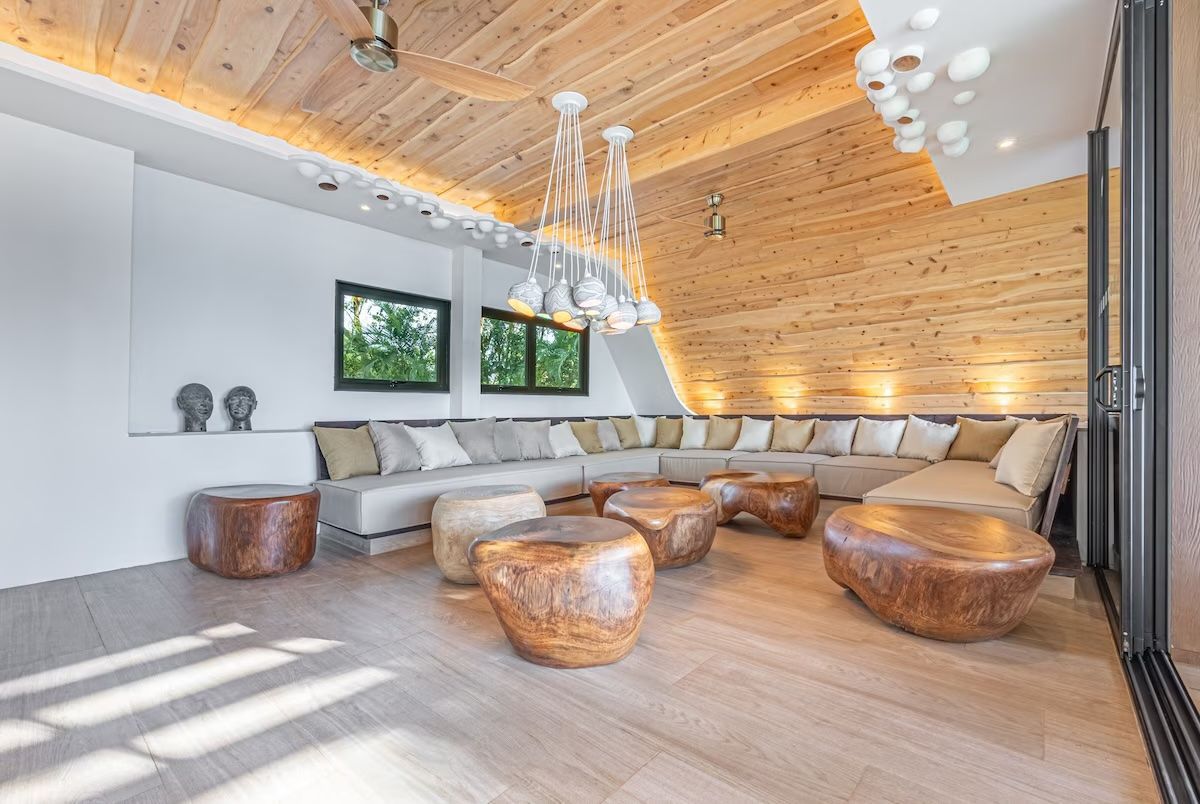 Salon spacieux et moderne avec des touches de bois, un canapé intégré, des tables basses originales et des suspensions lumineuses.