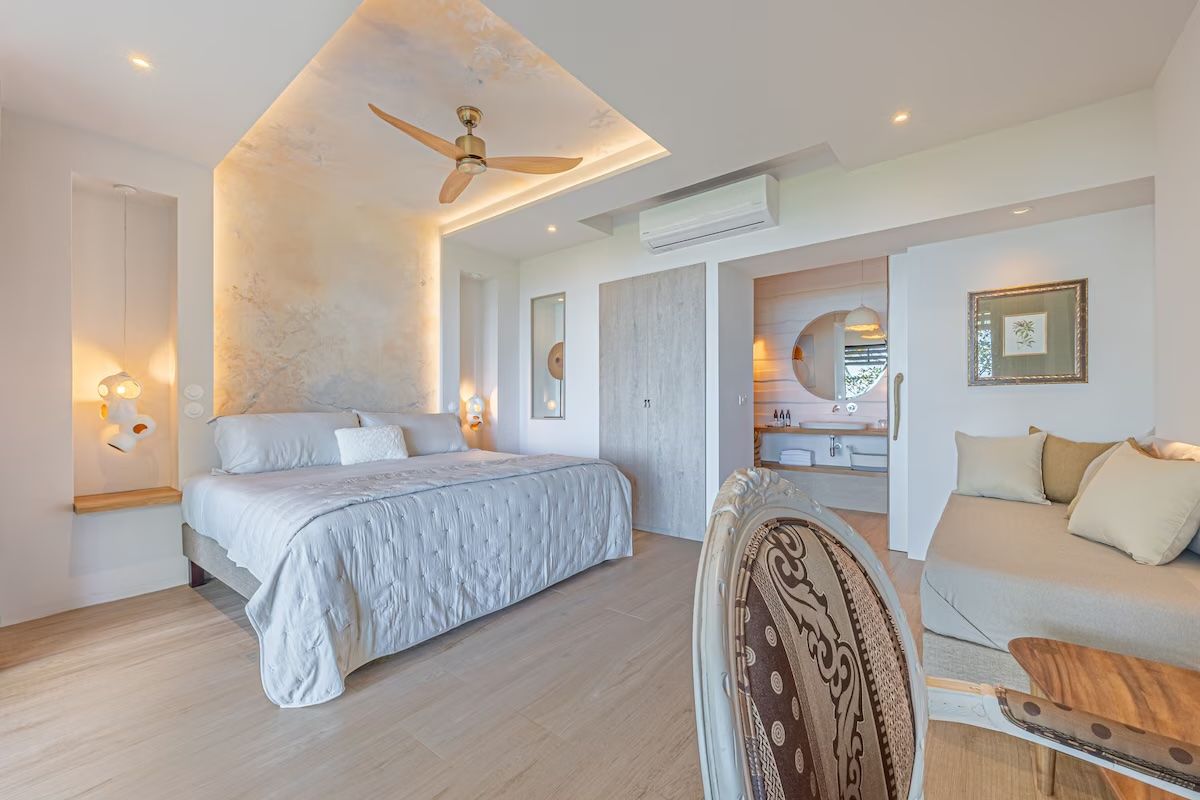 Chambre avec grand lit, coin salon et salle de bains attenante. Le bois clair et les tons neutres créent une atmosphère relaxante.