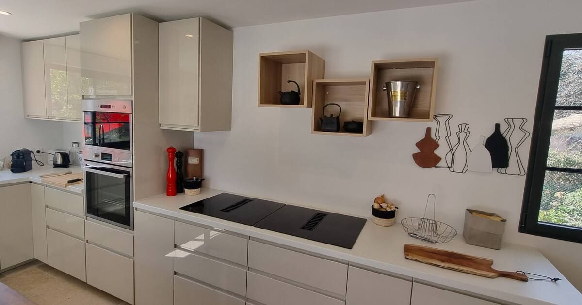 Cuisine moderne avec placards blancs, électroménager intégré et étagères flottantes en bois.
