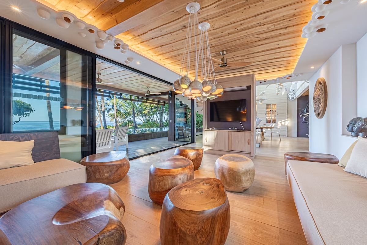 Coin salon avec mobilier en bois, portes coulissantes en verre, vue sur l'océan et éclairage décoratif au plafond.