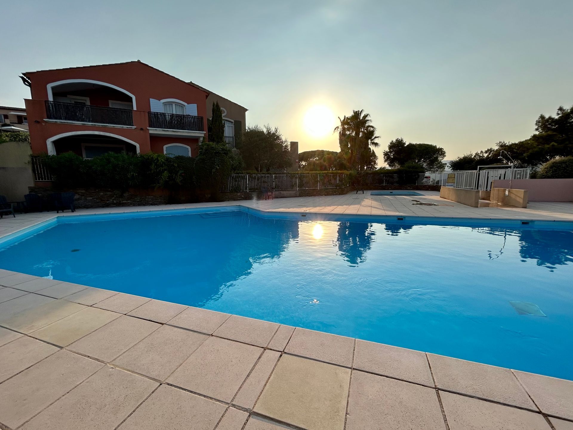 Piscine à l'eau bleue devant une maison. Le soleil brille de mille feux dans le ciel.