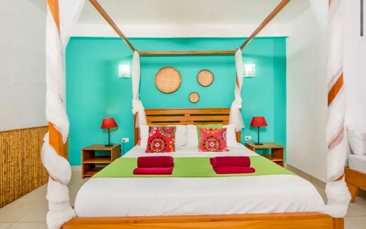 Chambre avec lit à baldaquin, mur turquoise, décorations tissées et touches de rouge.