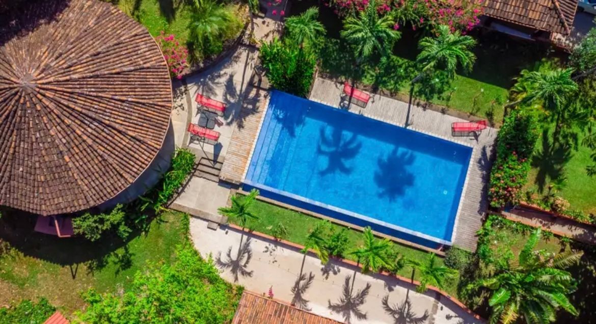 Vue aérienne d'une piscine entourée de verdure et de bâtiments aux toits de tuiles brunes.