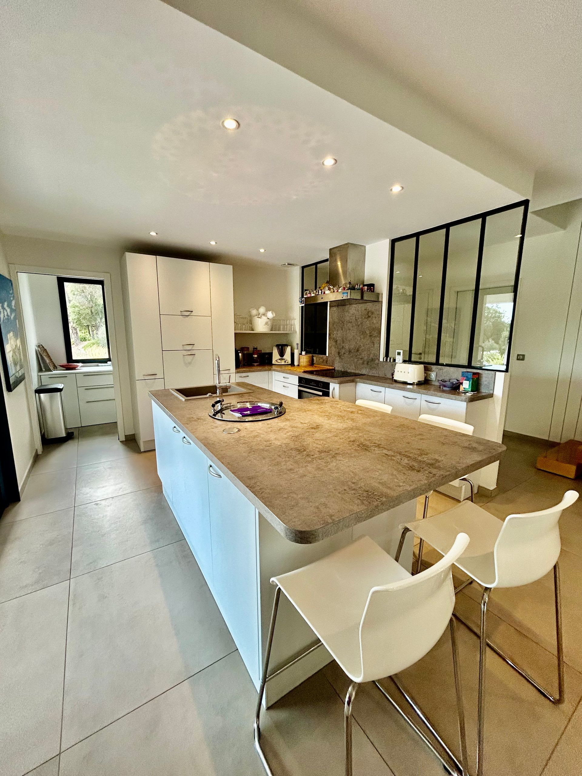 Cuisine blanche moderne avec îlot central, coin repas et paroi vitrée.