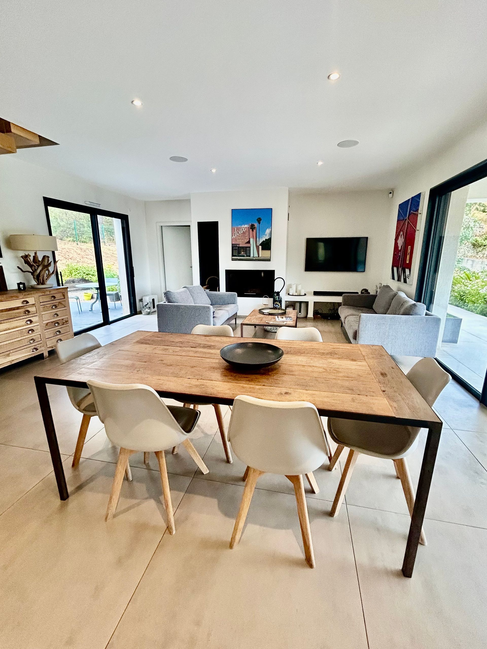 Coin repas avec table en bois, chaises et portes ouvertes sur l'extérieur.